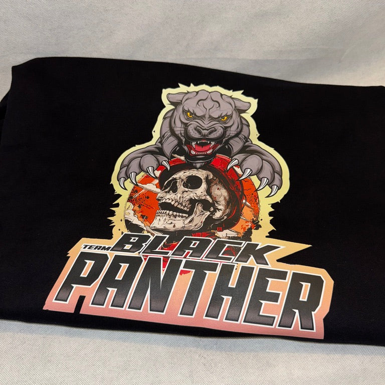 A folded black t-shirt featuring a large graphic print of a fierce black panther holding a skull, with the text 'TEAM BLACK PANTHER' below it, displayed on a light gray fabric background.