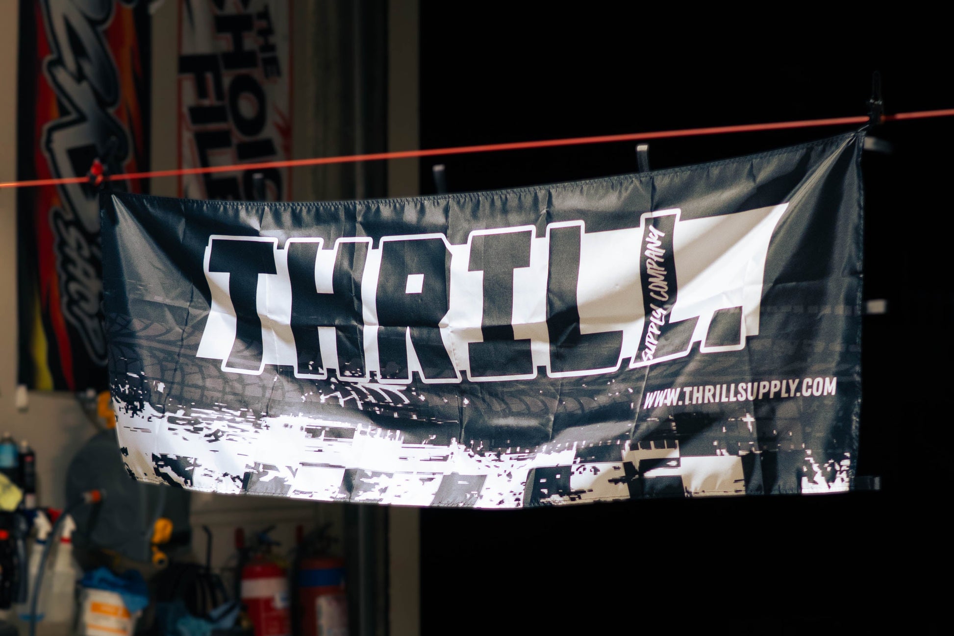 A black and white Thrill Racing banner hanging from a red rope in a garage setting.